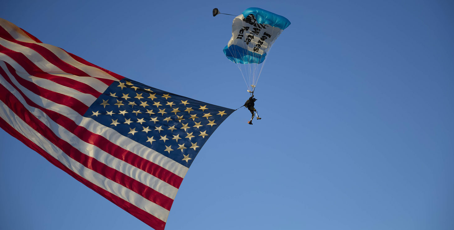 Un veterano que lleva un paracaídas presenta la bandera estadounidense que cae del cielo.